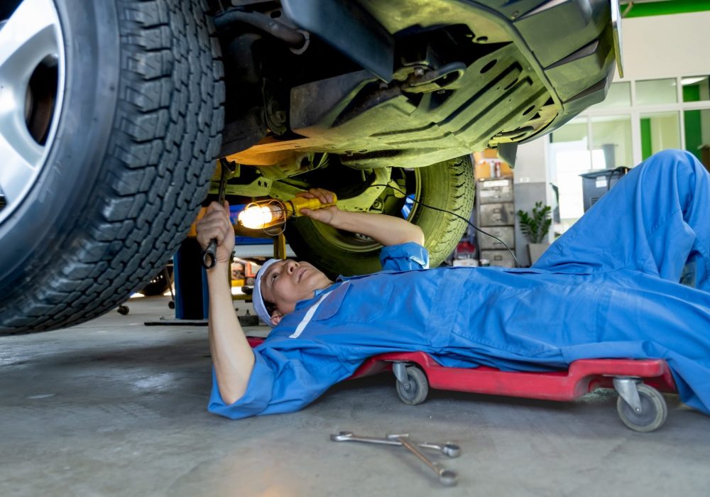 Technician or garage worker lie down under the car and use lantern to guide for fix the problem