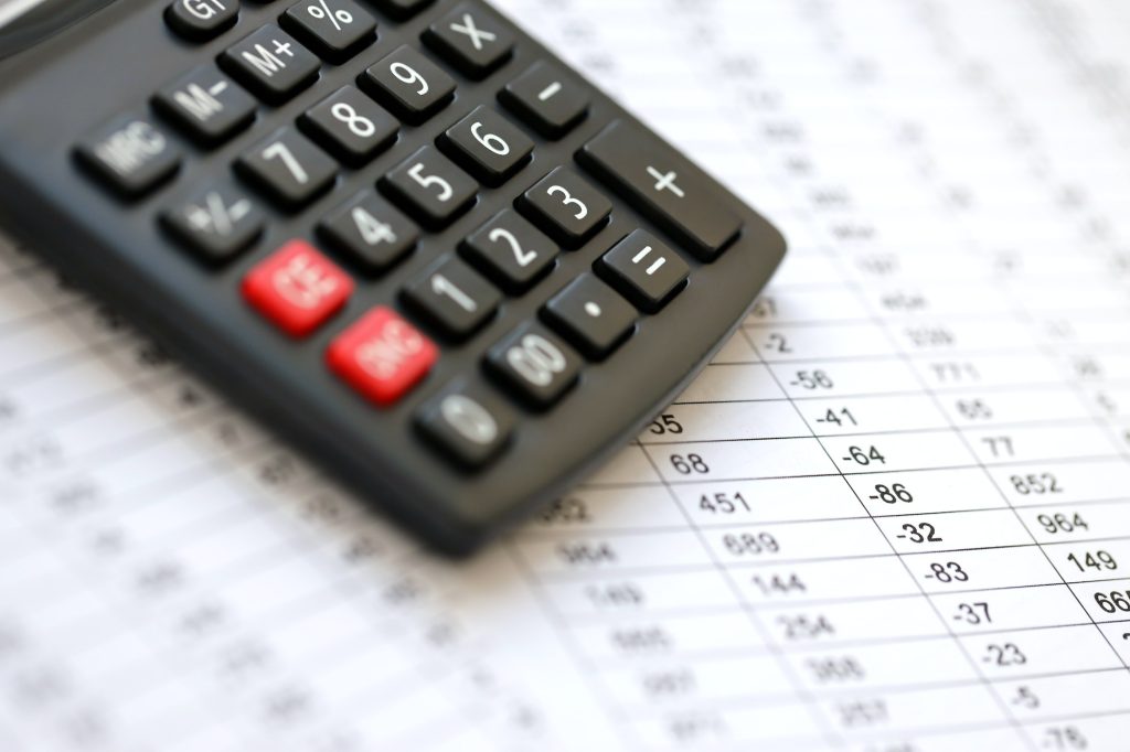 Big black calculator lies on financial statement and balance sheeet on desk of auditor close up