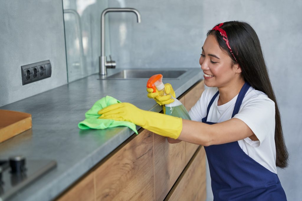 Happy young woman, cleaning lady smiling while cleaning the kitchen