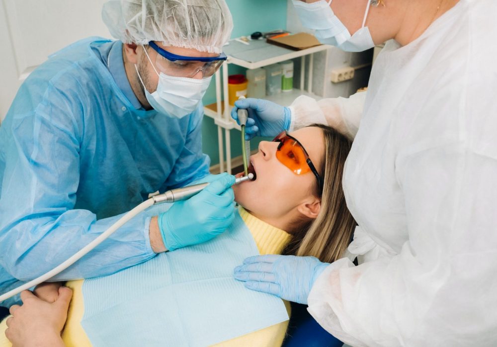 A male dentist with dental tools drills the teeth of a patient with an assistant. The concept of