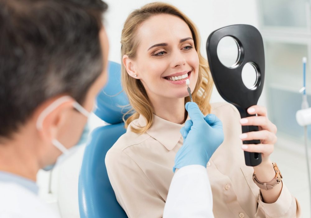Female patient choosing tooth implant looking at mirror in modern dental clinic