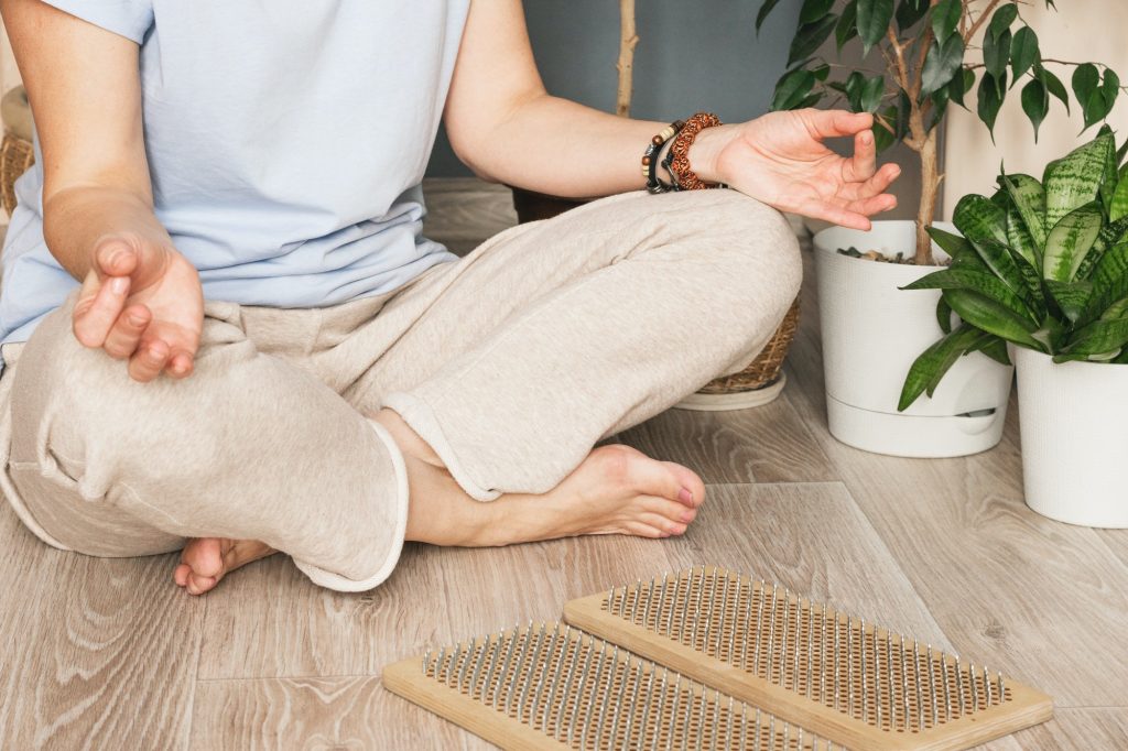 Woman sits on the floor in Yoga posture, a wooden sadhu board with nails, for sadhu practice at home